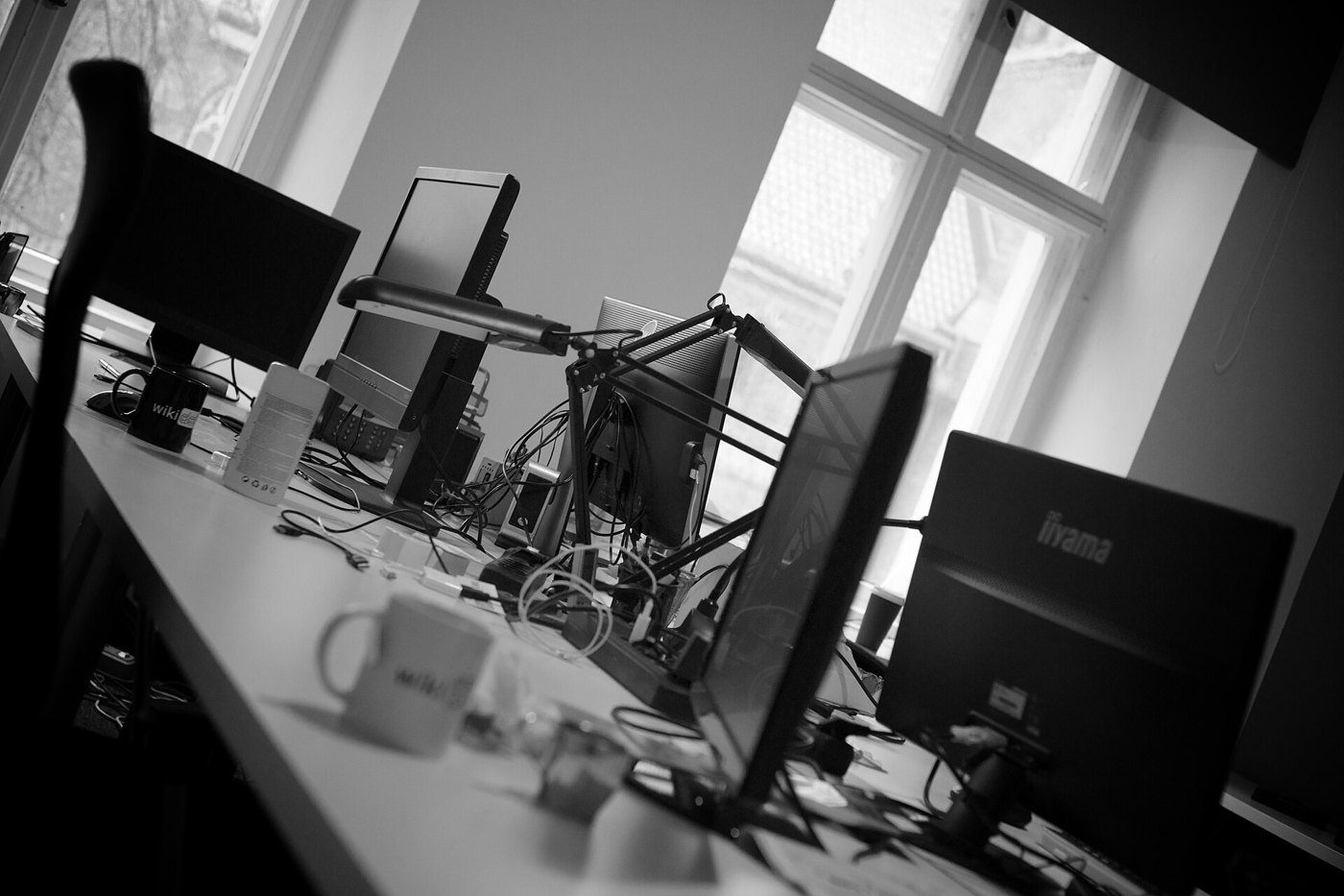 Rangee de postes de travail et d ecrans laisses allumes dans un bureau, vus en noir et blanc