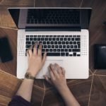 Mains sur le clavier d'un ordinateur portable vu de dessus sur un bureau en bois