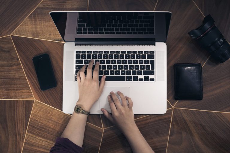 Mains sur le clavier d'un ordinateur portable vu de dessus sur un bureau en bois
