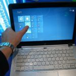 Doigt sur l'écran tactile d'un ordinateur portable affichant l'écran d'accueil de Windows