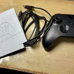 Manette sans fil Xbox noire posee sur un etabli a cote de son cable USB type A vers type C enroule
