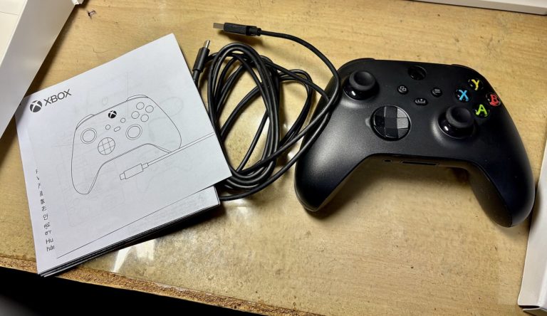 Manette sans fil Xbox noire posee sur un etabli a cote de son cable USB type A vers type C enroule