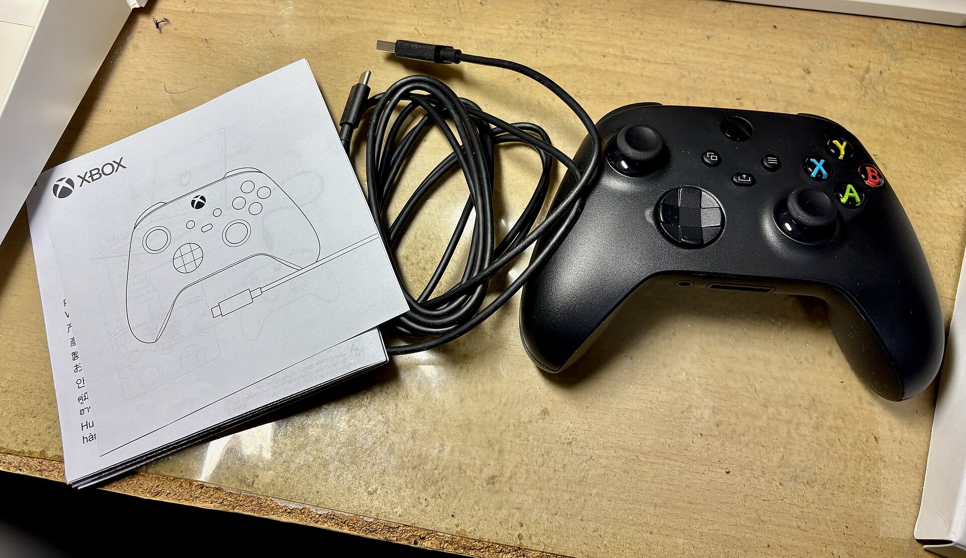 Manette sans fil Xbox noire posee sur un etabli a cote de son cable USB type A vers type C enroule