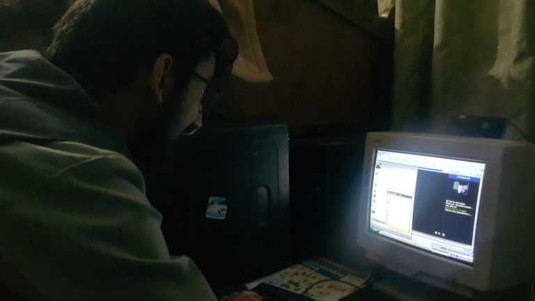 Personne assise devant un ordinateur de bureau ancien, ecran et clavier sur un plan de travail