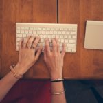 Mains tapant du texte sur un clavier d'ordinateur portable pose sur un bureau