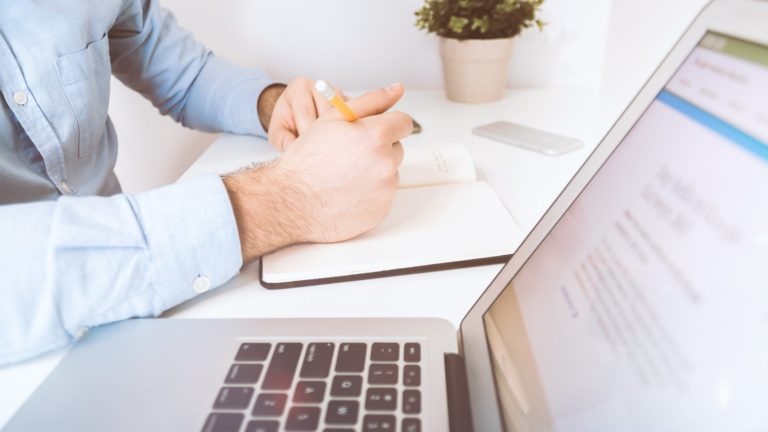 Porteur de projet qui prend des notes devant son ordinateur avant de lancer son projet web